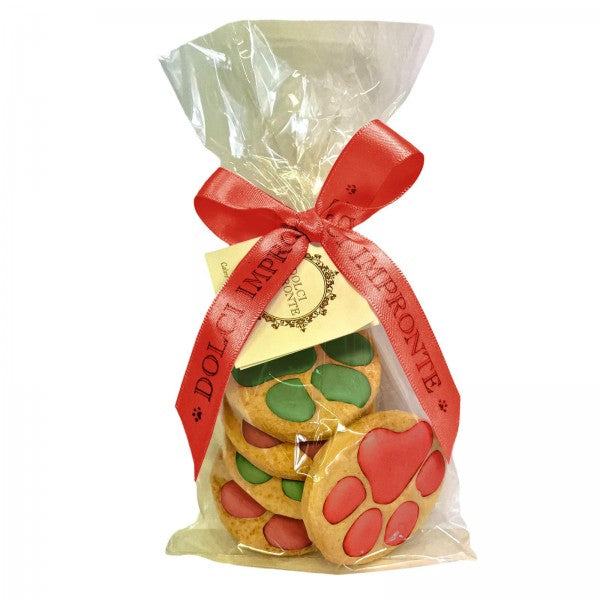 Biscuit artisanal de Noël pour chien en forme de pattes, décoré de glaçage rouge et vert, emballé dans un sachet avec ruban personnalisé Dolci Impronte.